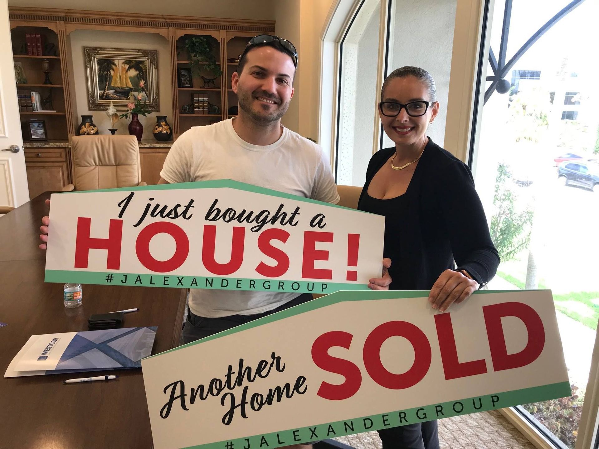 A man and a woman are holding signs that say i just bought a house and another home sold.