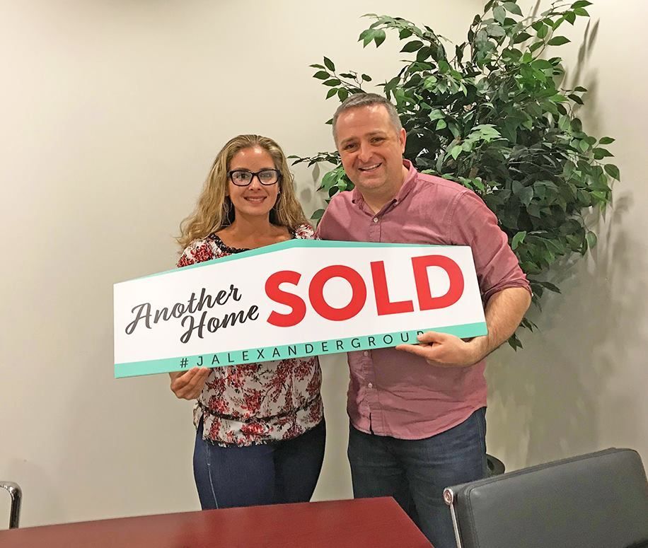 A man and a woman are holding a sold sign.