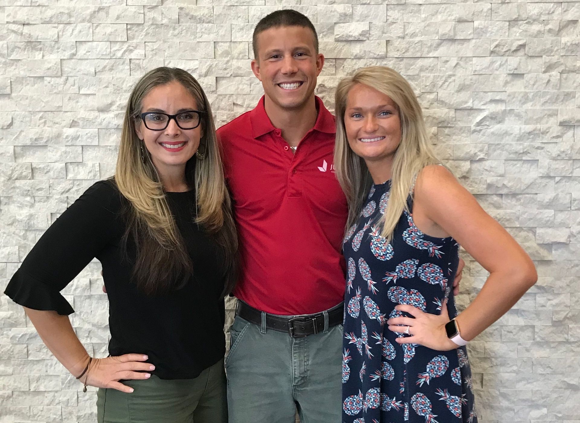 A man and two women are posing for a picture in front of a brick wall.