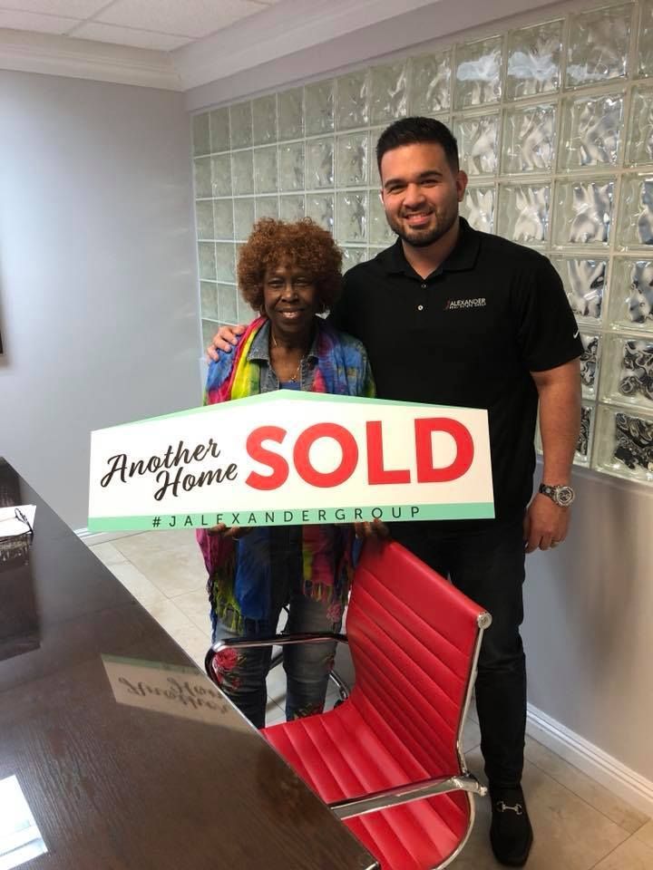 A man and a woman are standing next to each other holding a sold sign.