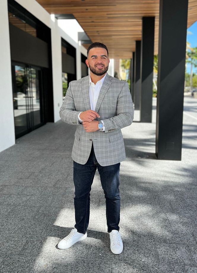 A man in a suit and white sneakers is standing in front of a building.