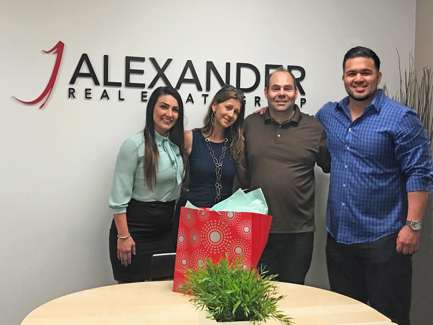 A group of people are posing for a picture in front of a sign that says alexander real estate