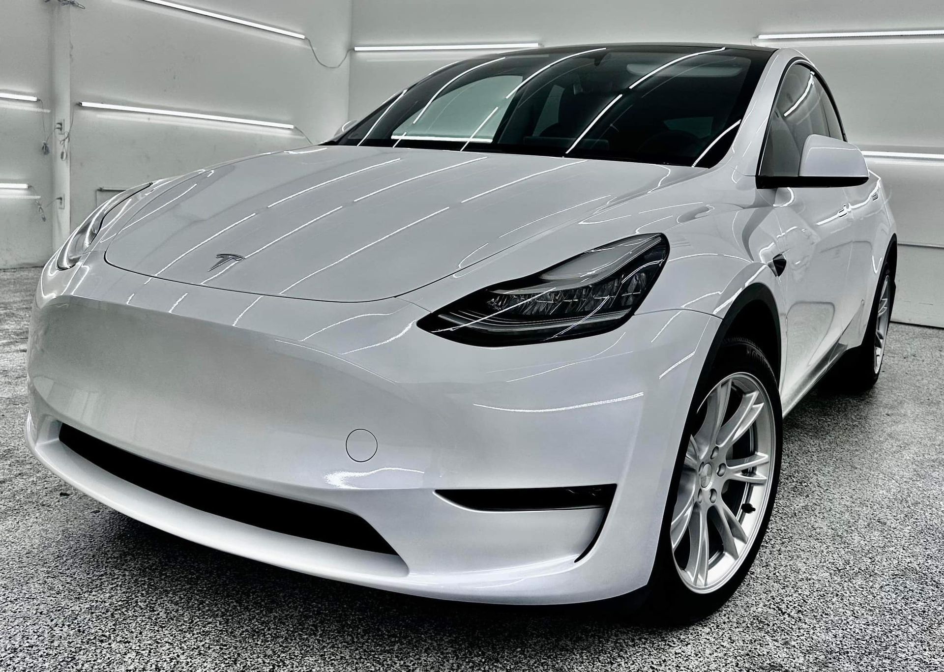 A white tesla model y is parked in a garage.