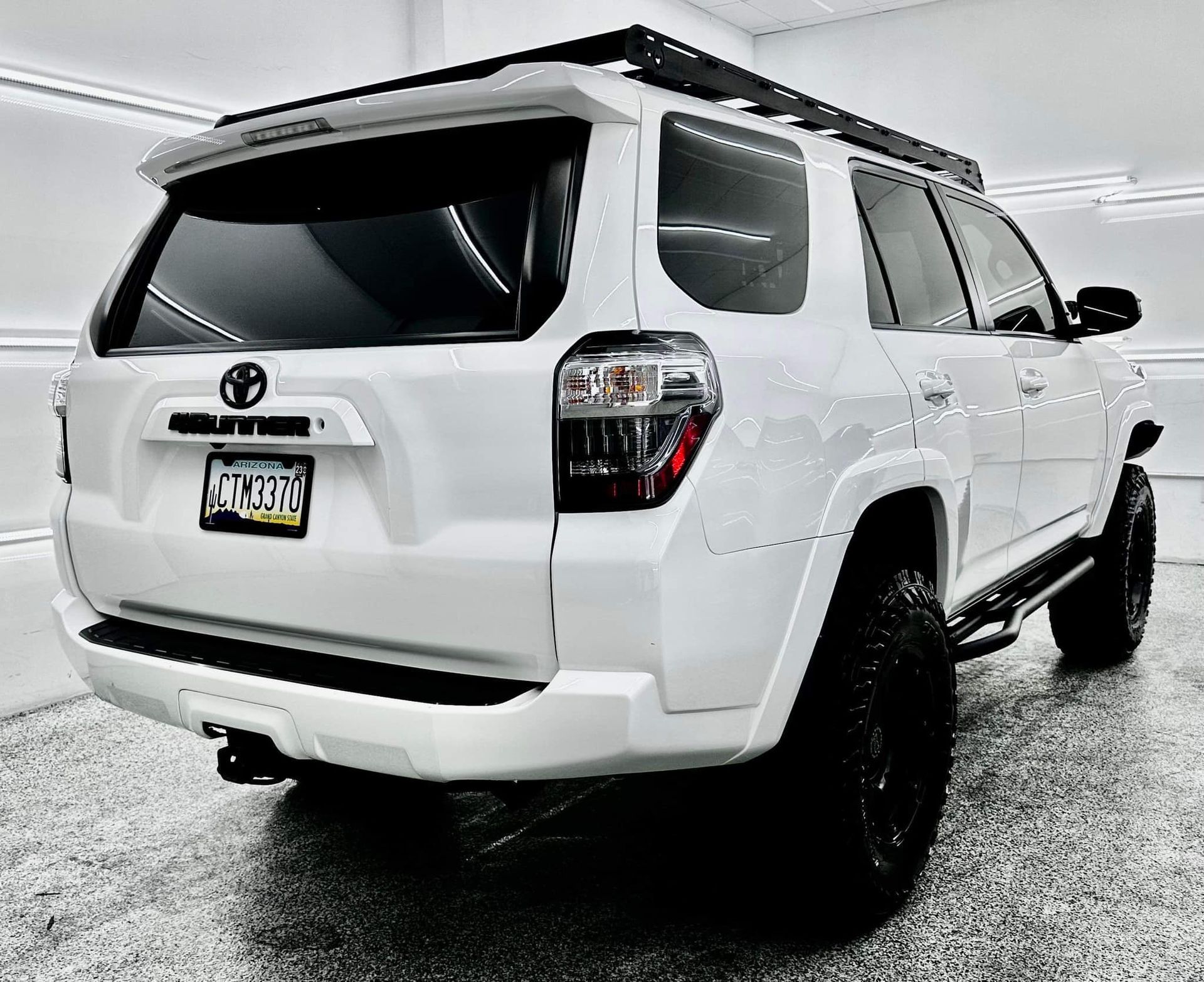 A white toyota 4runner with a roof rack is parked in a garage.
