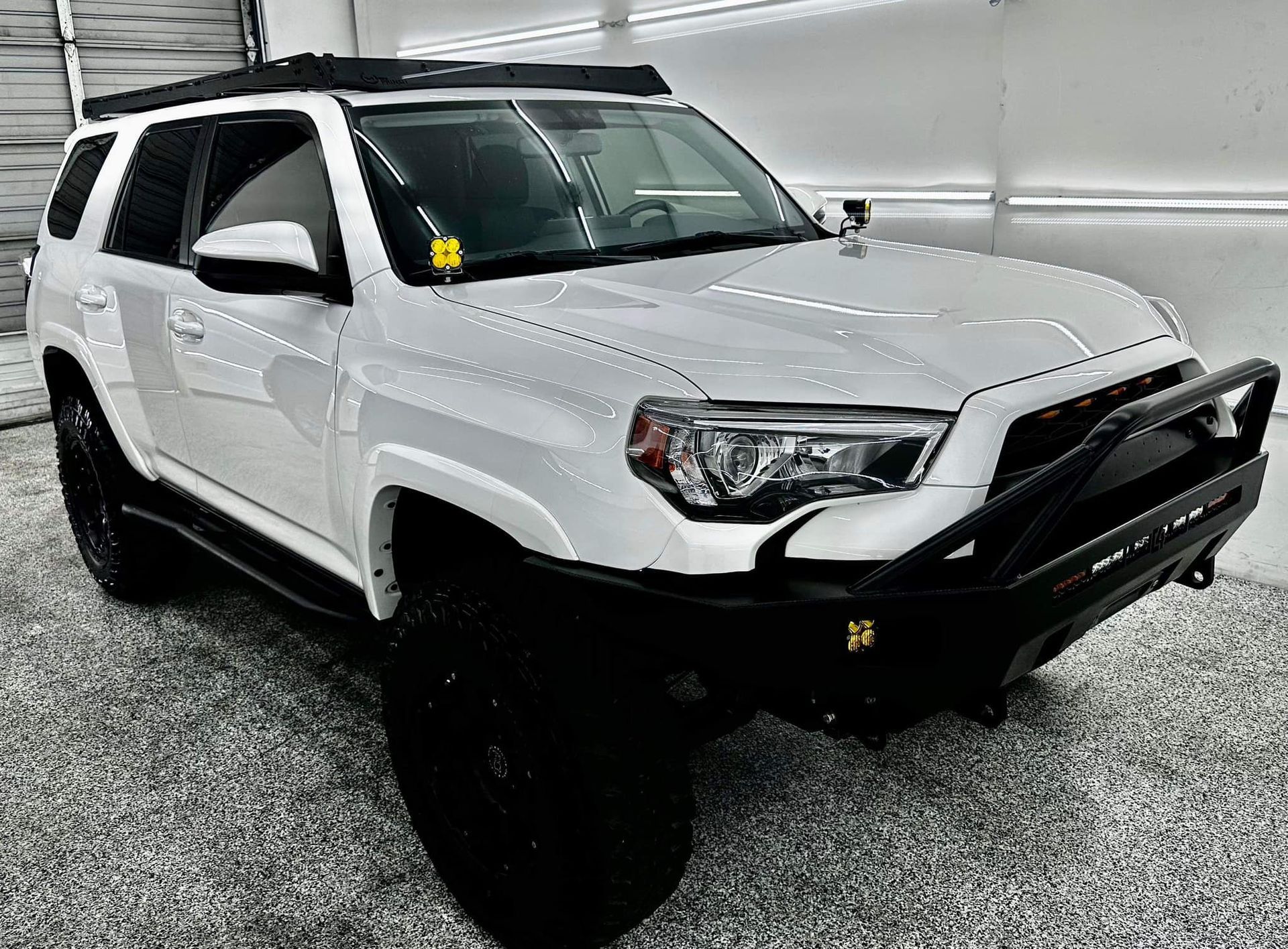 A white toyota 4runner with a roof rack is parked in a garage.