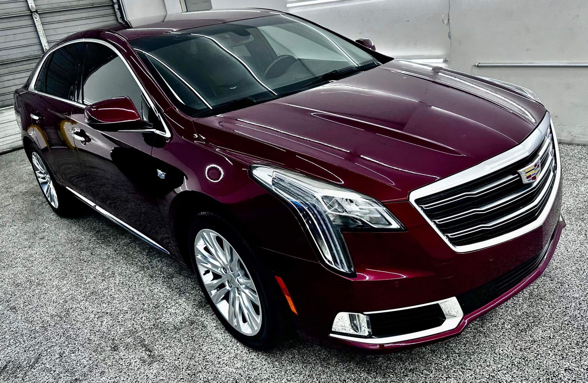 A red cadillac is parked in a gravel lot