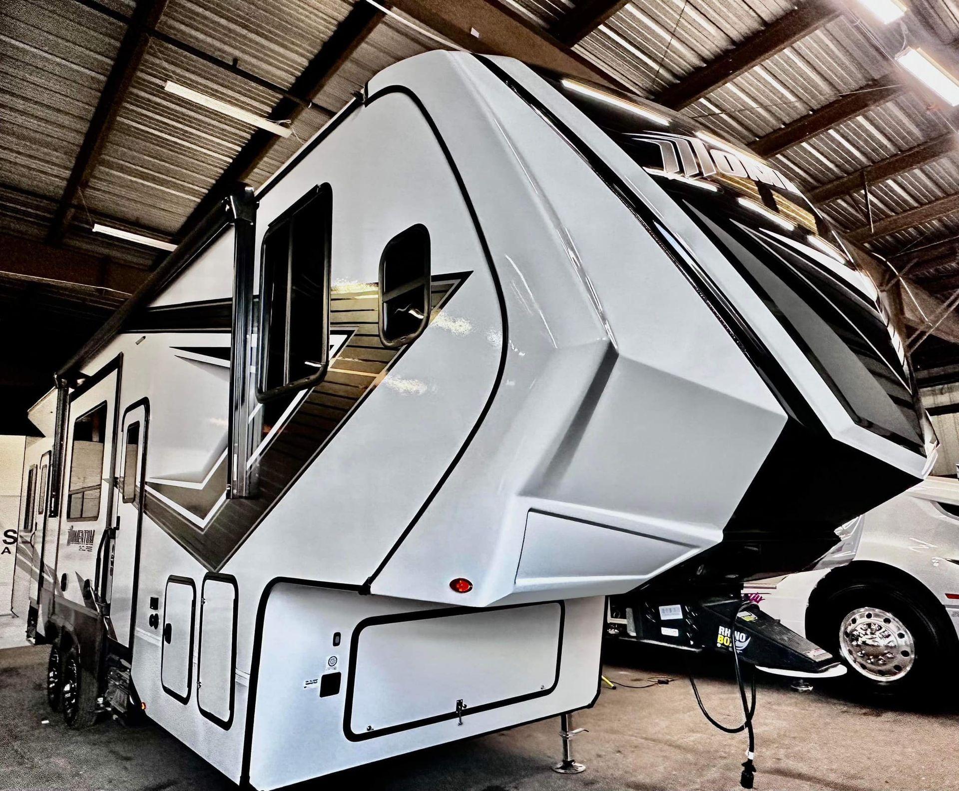 A white rv is parked in a garage next to a car with Bob Moses ceramic coating, Sensha World Crystal Glow