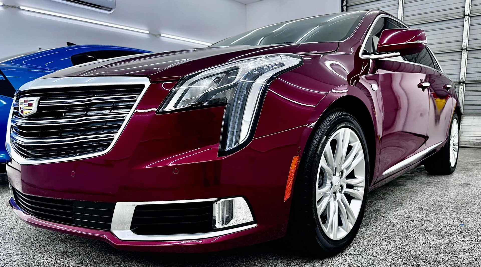 A red cadillac is parked in a garage next to a blue car.
