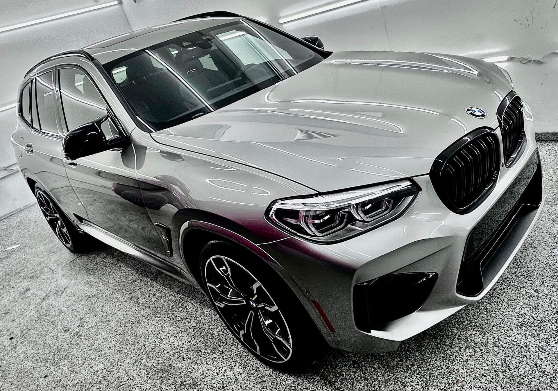 A silver bmw x3 m is parked in a garage.