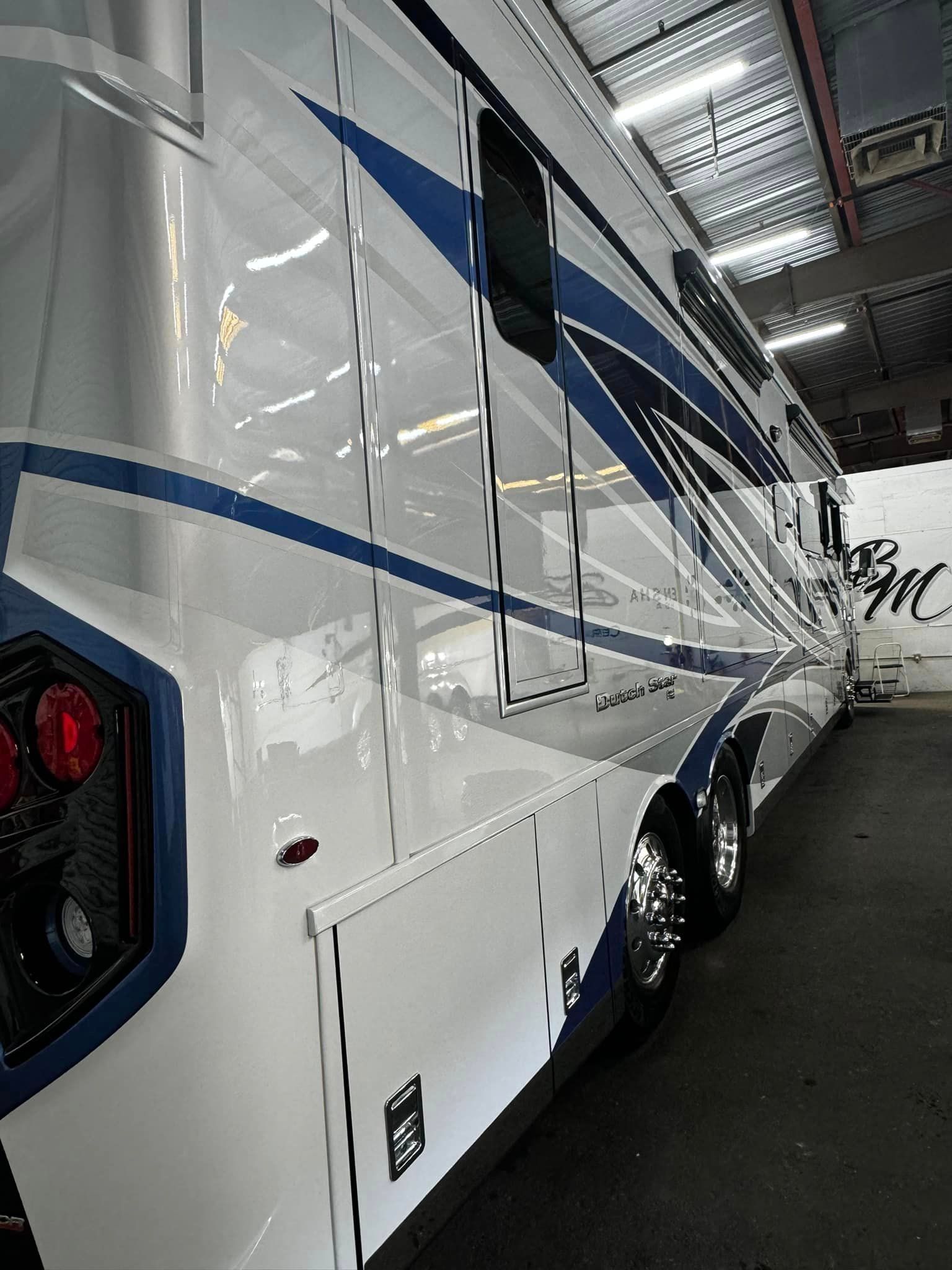 A large white and blue rv is parked in a garage with Bob Moses ceramic coating, Sensha World Crystal Glow