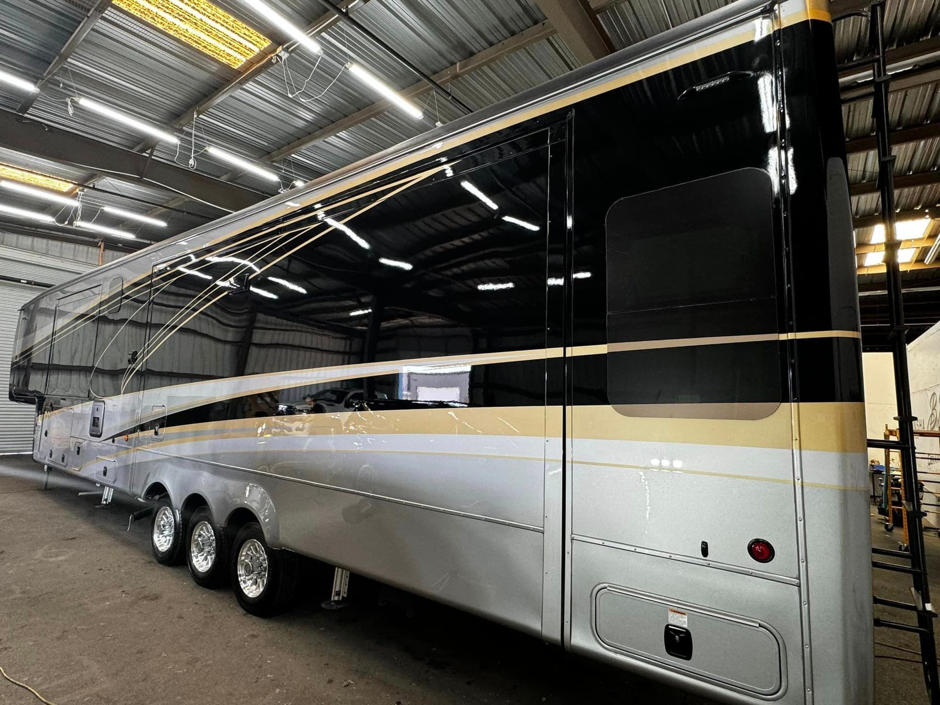 A large silver and gold bus is parked in a warehouse with Bob Moses ceramic coating, Sensha World Crystal Glow