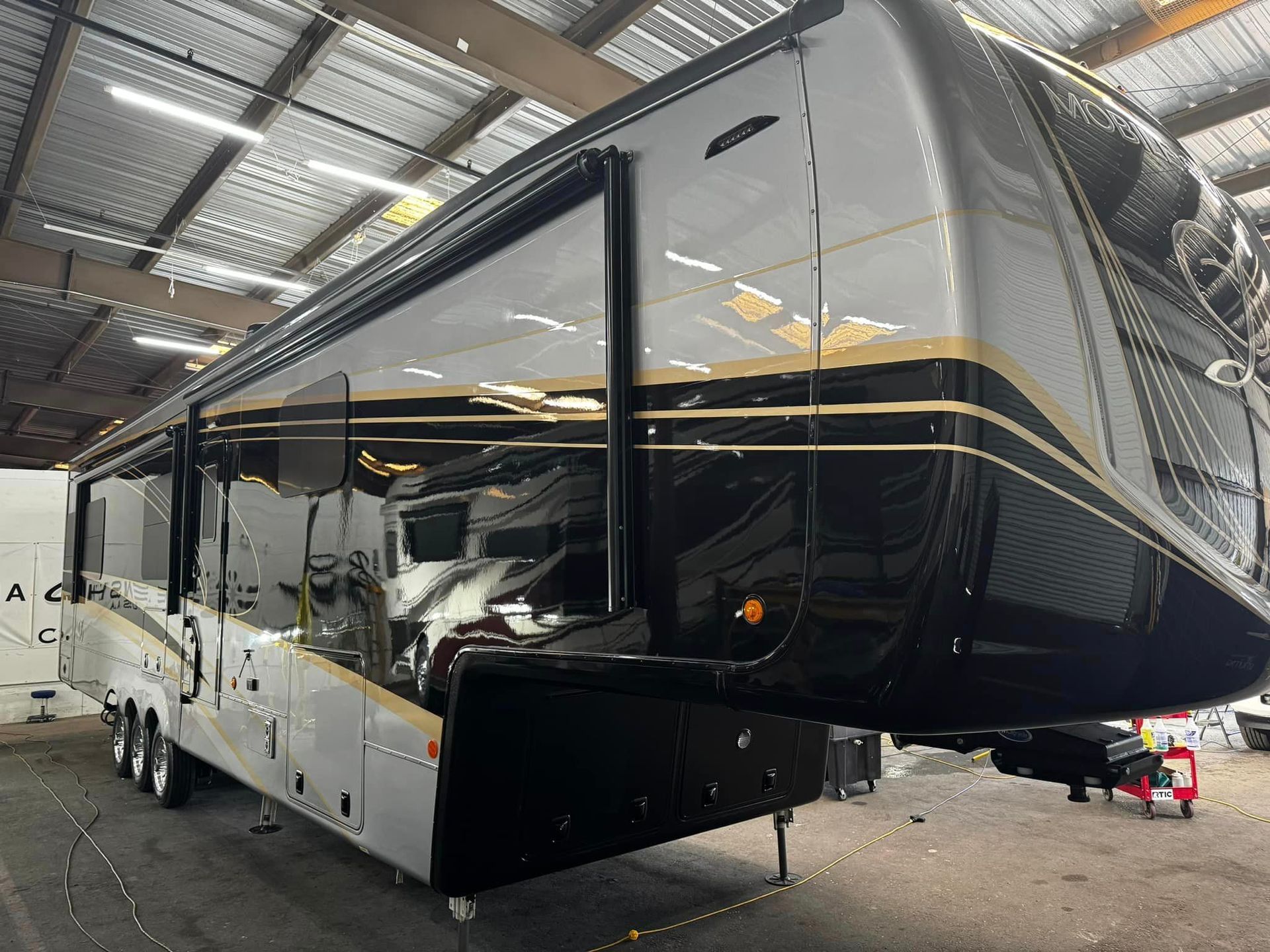 A large black and white rv is parked in a garage with Bob Moses ceramic coating, Sensha World Crystal Glow