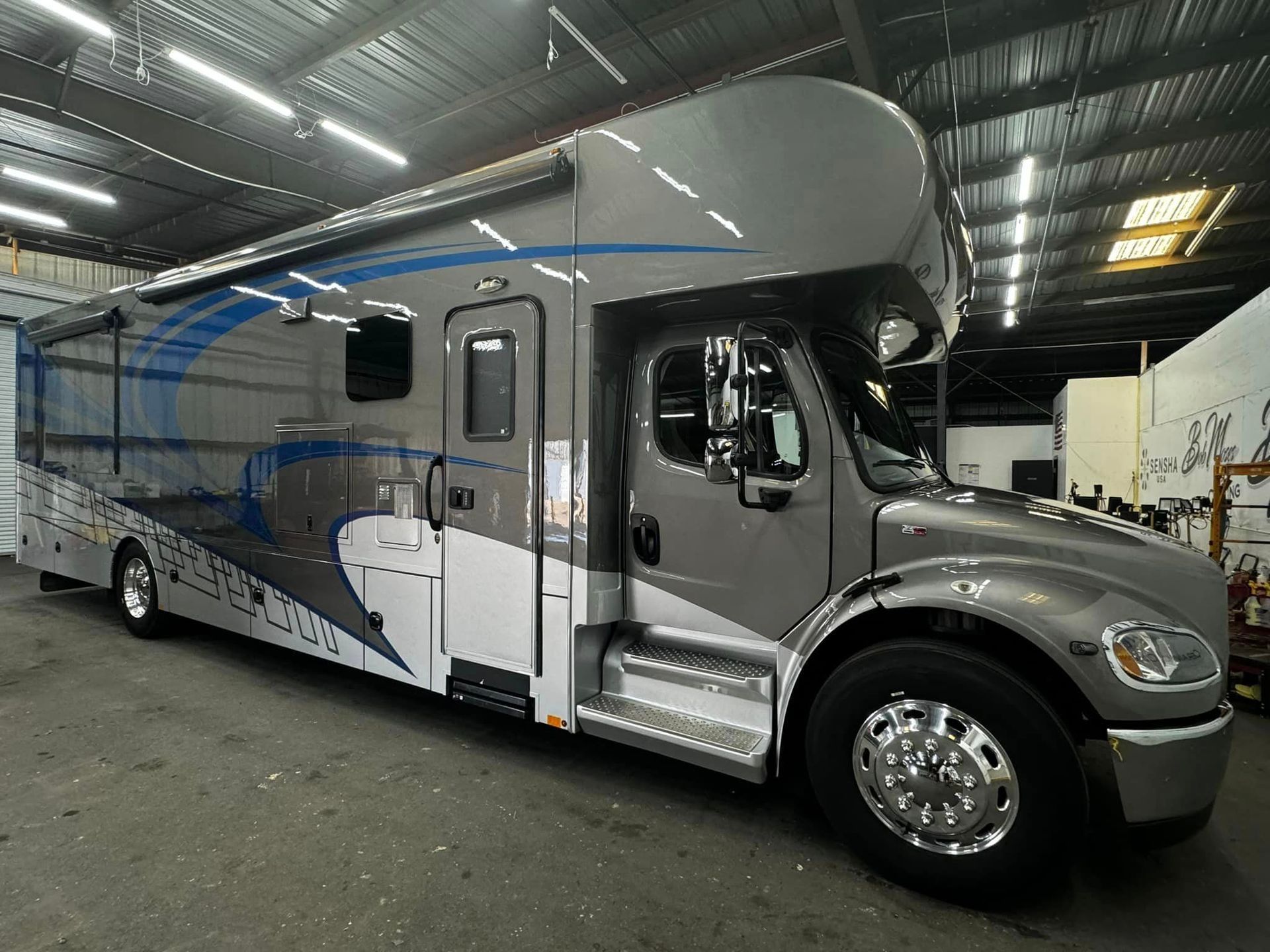 A large gray and white rv is parked in a garage with Bob Moses ceramic coating, Sensha World Crystal Glow