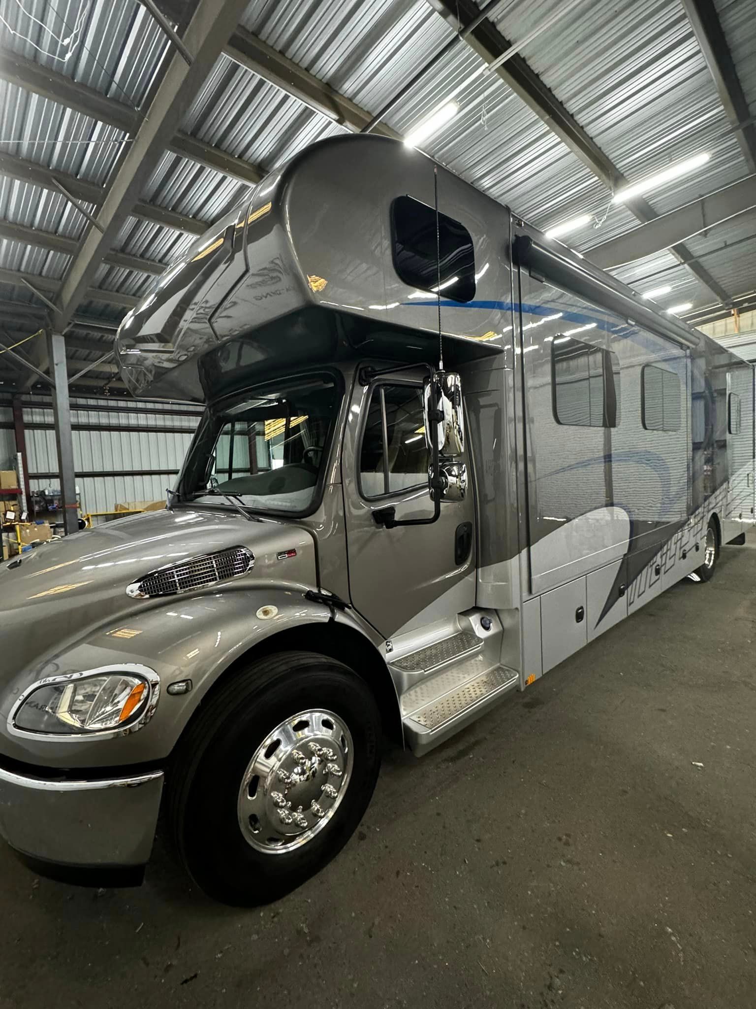 A large silver rv is parked in a warehouse with Bob Moses ceramic coating, Sensha World Crystal Glow