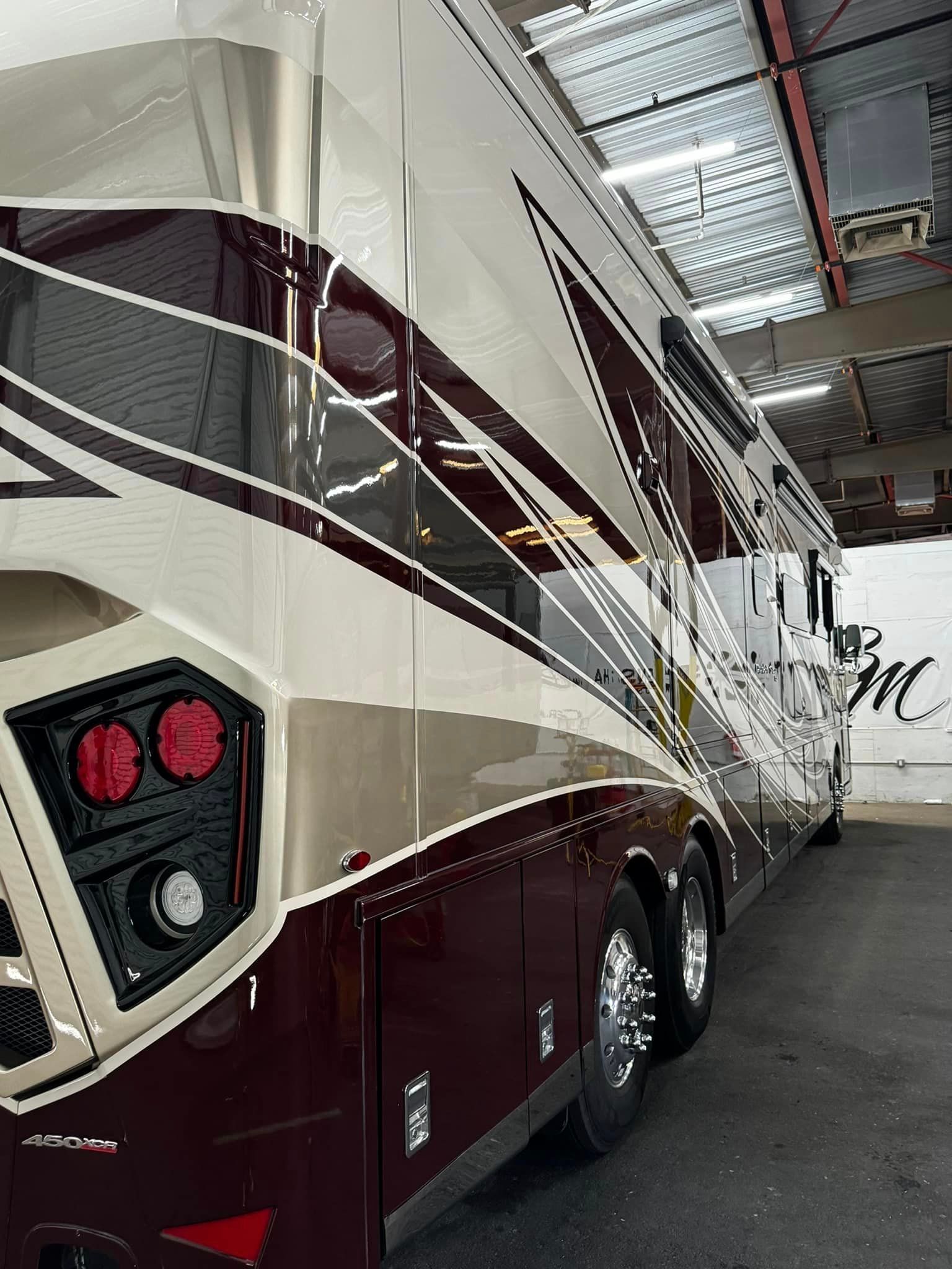 A large red and white bus is parked in a garage with Bob Moses ceramic coating, Sensha World Crystal Glow