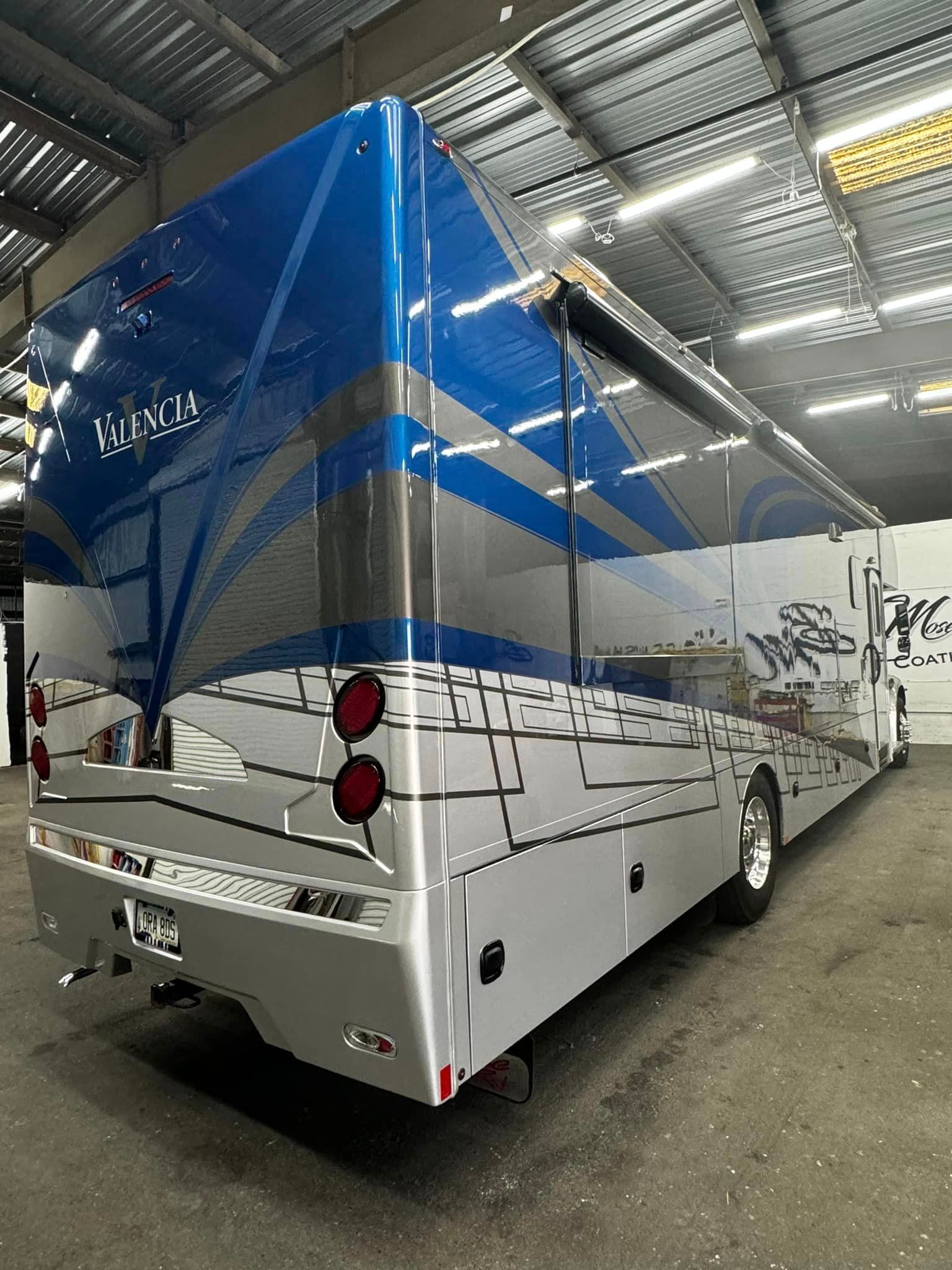 A large blue and white bus is parked in a warehouse with Bob Moses ceramic coating, Sensha World Crystal Glow