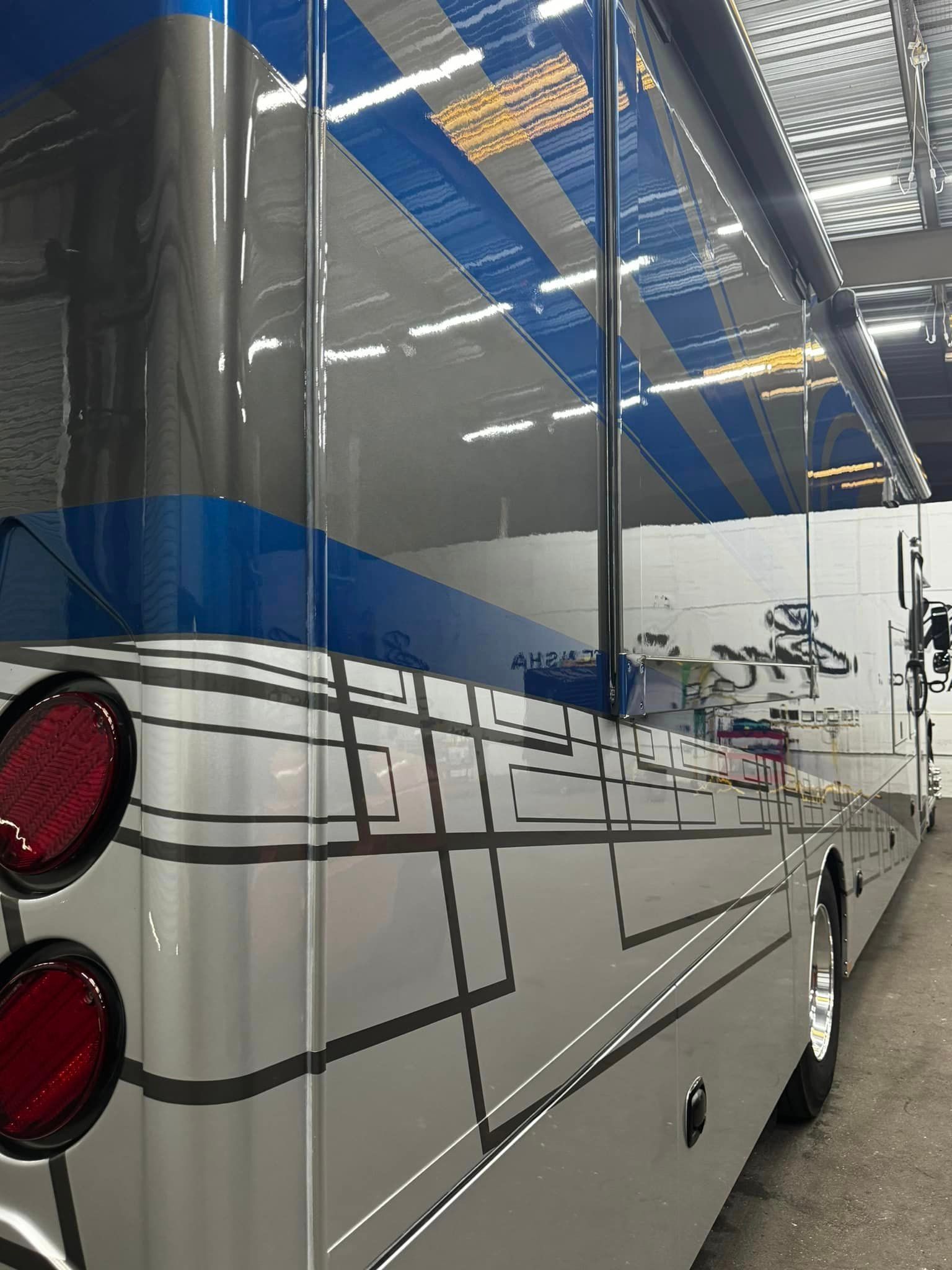 A silver and blue bus is parked in a warehouse with Bob Moses ceramic coating, Sensha World Crystal Glow