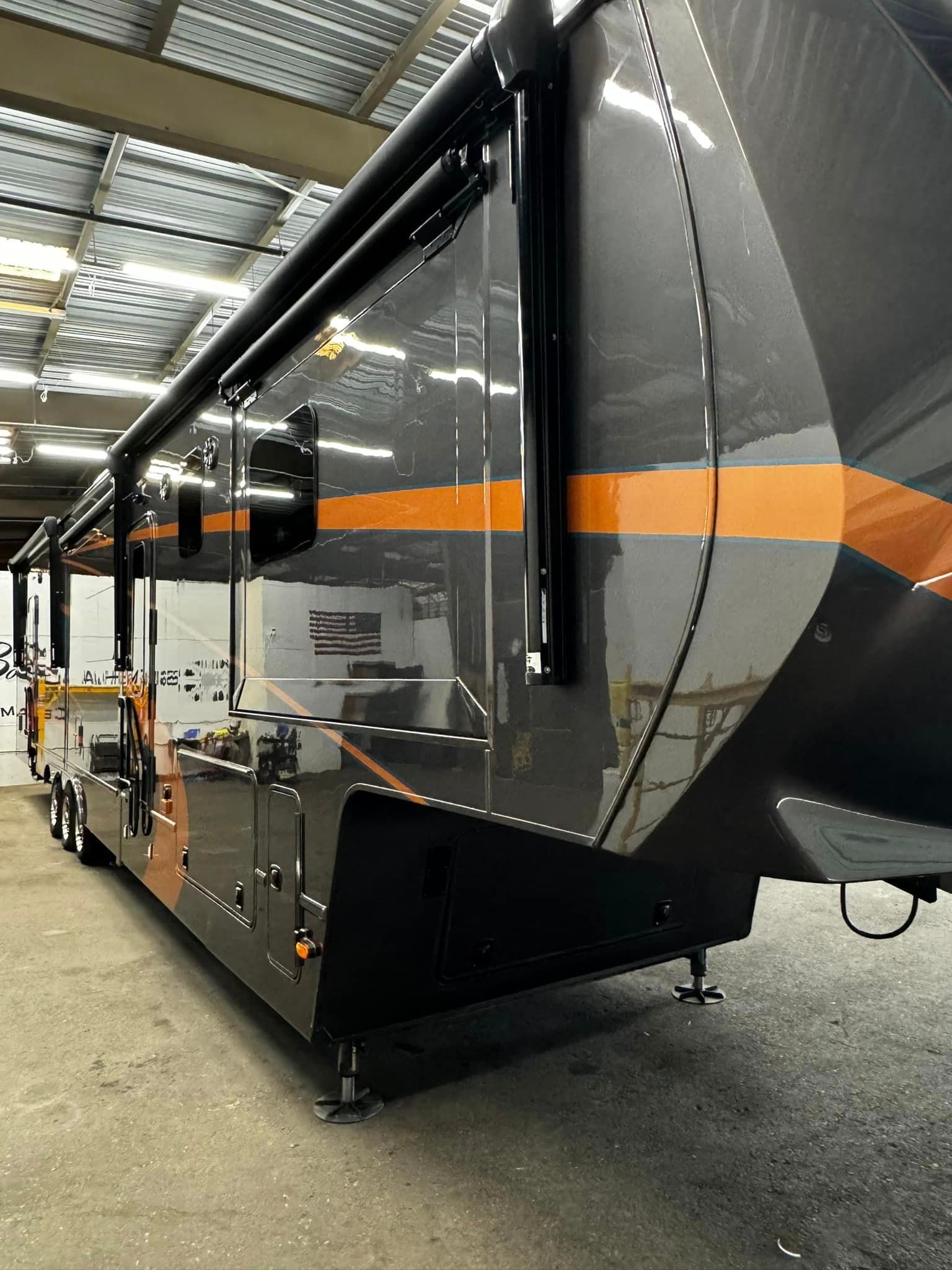 A large black and orange trailer is parked in a garage with Bob Moses ceramic coating, Sensha World Crystal Glow