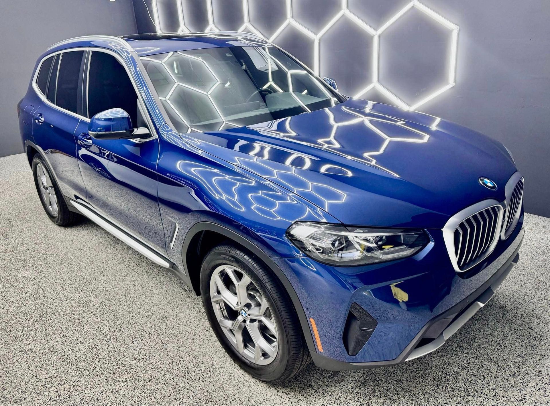 A blue bmw x3 is parked in a showroom.