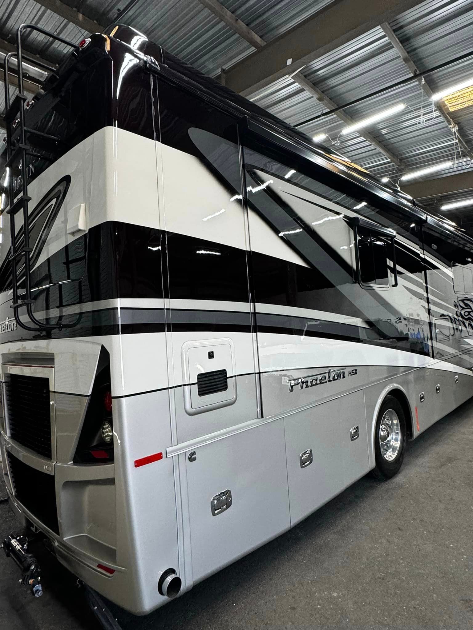 A large white and black rv is parked in a warehouse with Bob Moses ceramic coating, Sensha World Crystal Glow