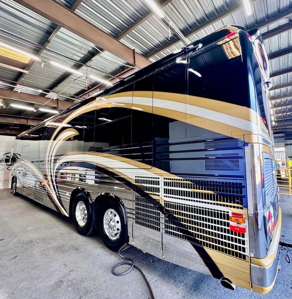A large black and gold bus is parked in a garage with Bob Moses ceramic coating, Sensha World Crystal Glow