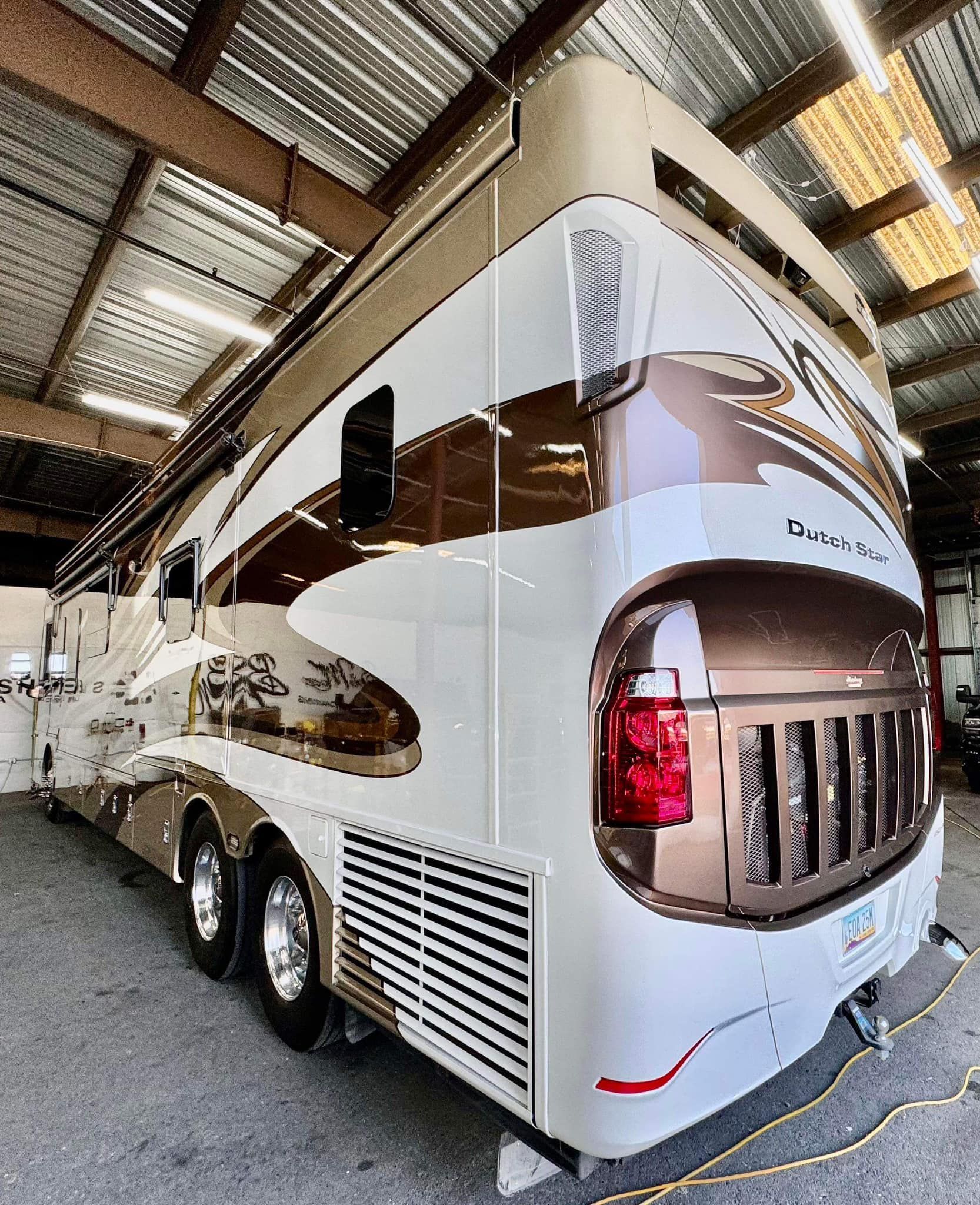A large white and brown rv is parked in a garage with Bob Moses ceramic coating, Sensha World Crystal Glow