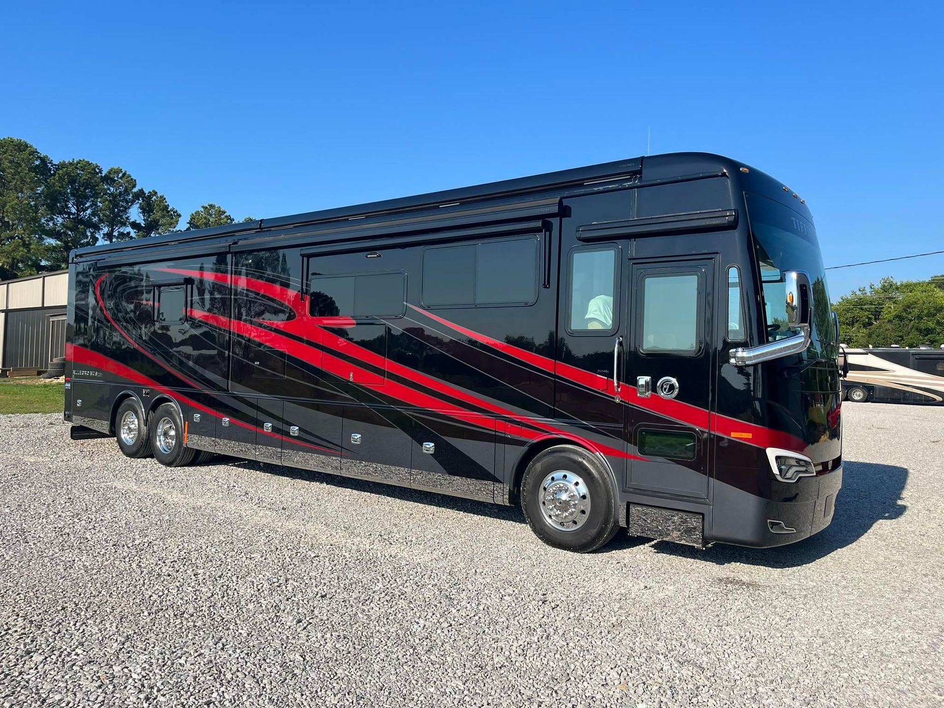 A large black and red rv is parked in a gravel lot with Bob Moses ceramic coating, Sensha World Crystal Glow