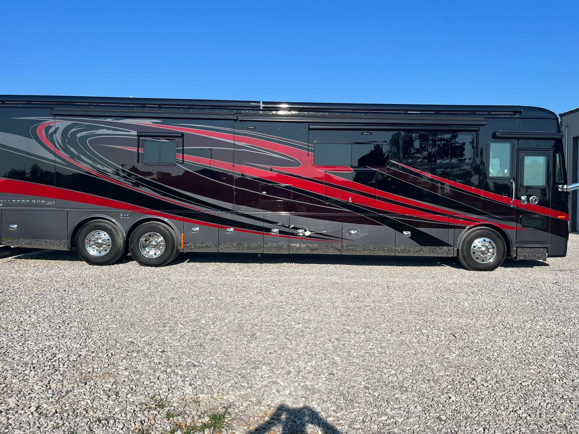 A large black and red rv is parked in a gravel lot with Bob Moses ceramic coating, Sensha World Crystal Glow