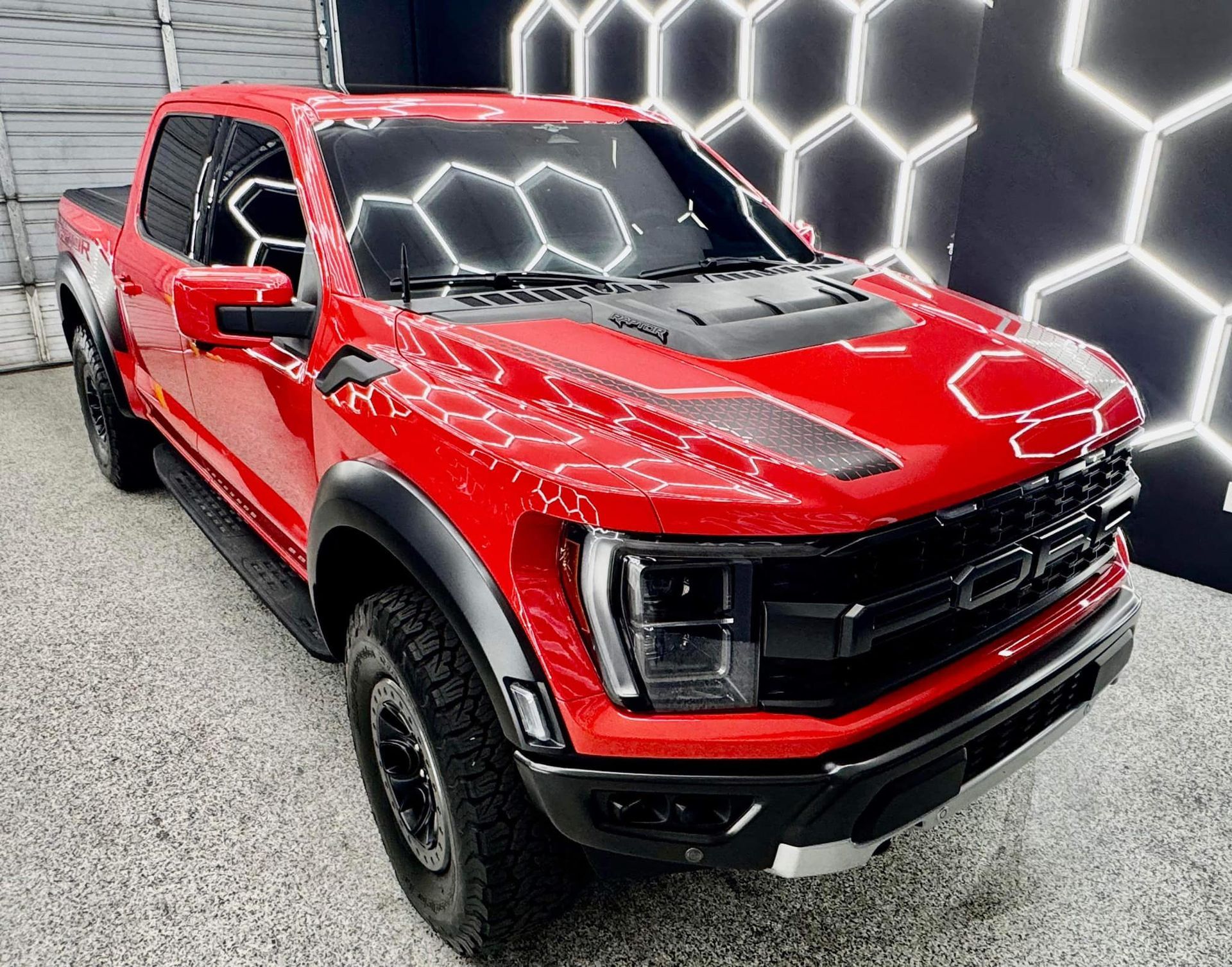 A red pickup truck is parked in front of a honeycomb wall with Bob Moses ceramic coating, Sensha World Crystal Glow