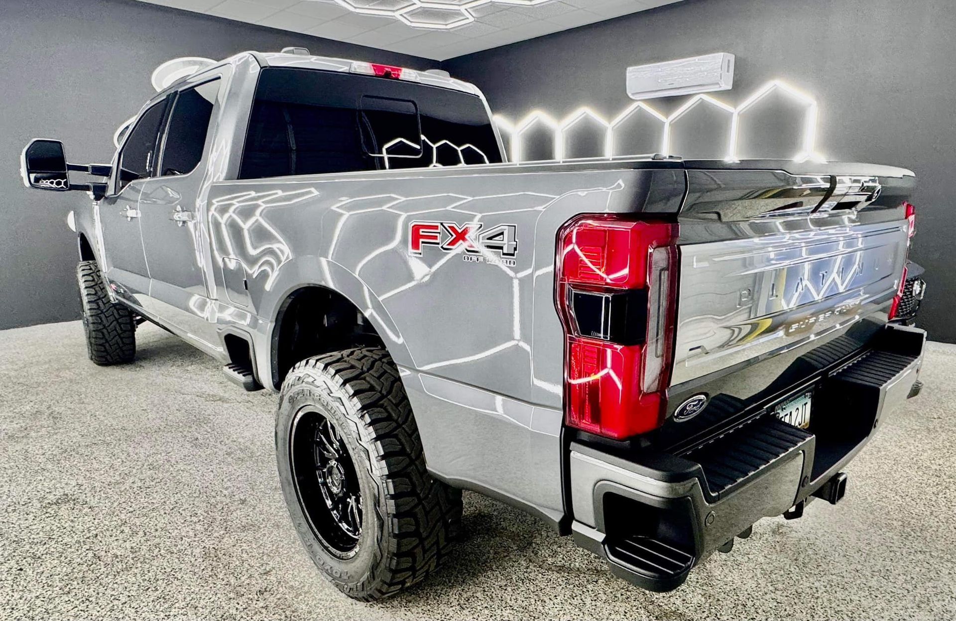 A gray truck is parked in a room with lights on the ceiling.