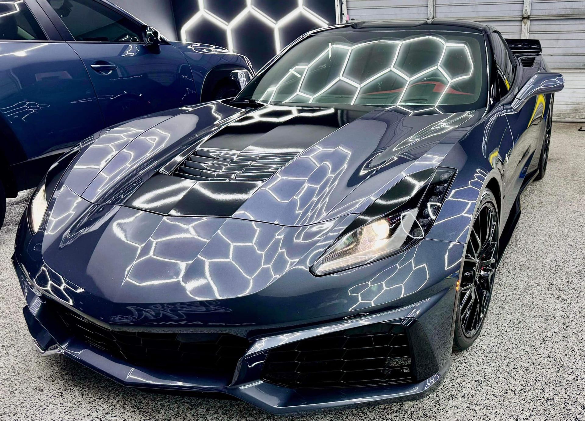 A black sports car is parked in front of a garage with Bob Moses ceramic coating, Sensha World Crystal Glow
