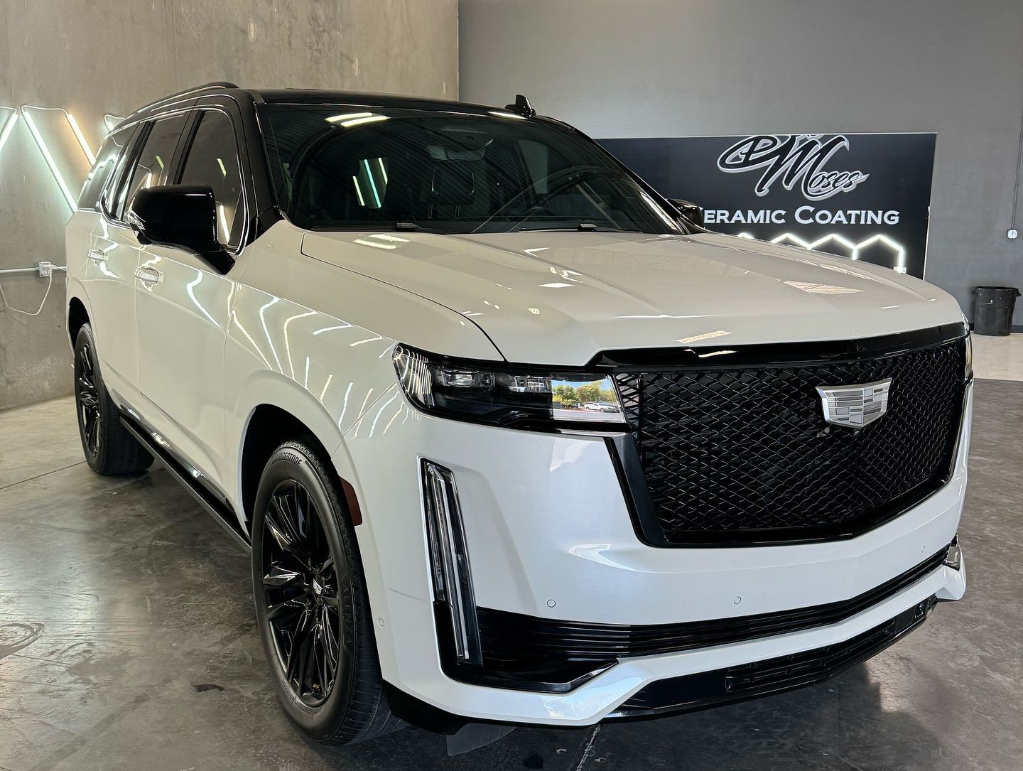 A white cadillac escalade is parked in a garage with Bob Moses ceramic coating, Sensha World Crystal Glow