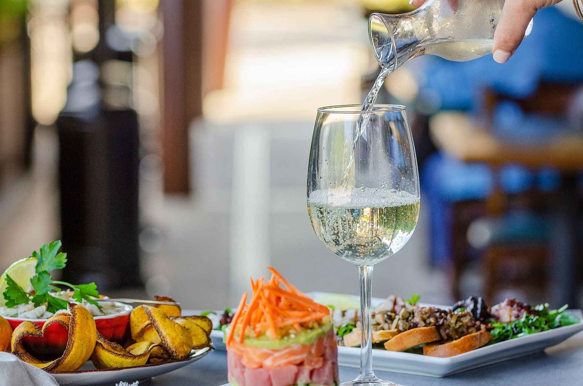 A person is pouring wine into a glass on a table with food.