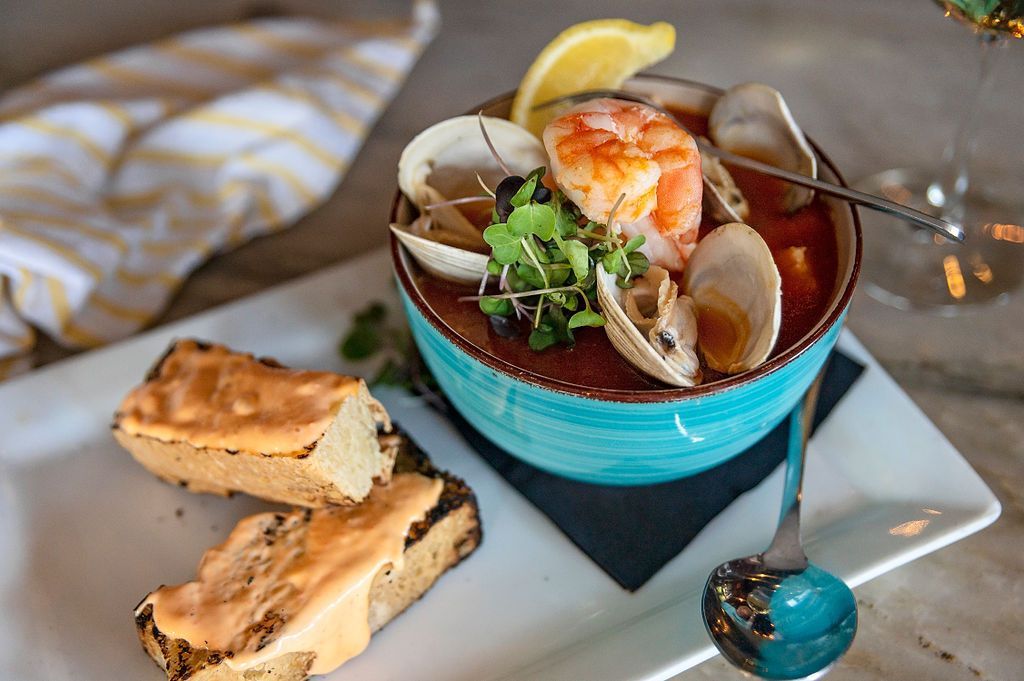 A bowl of seafood soup with bread and a spoon on a plate.