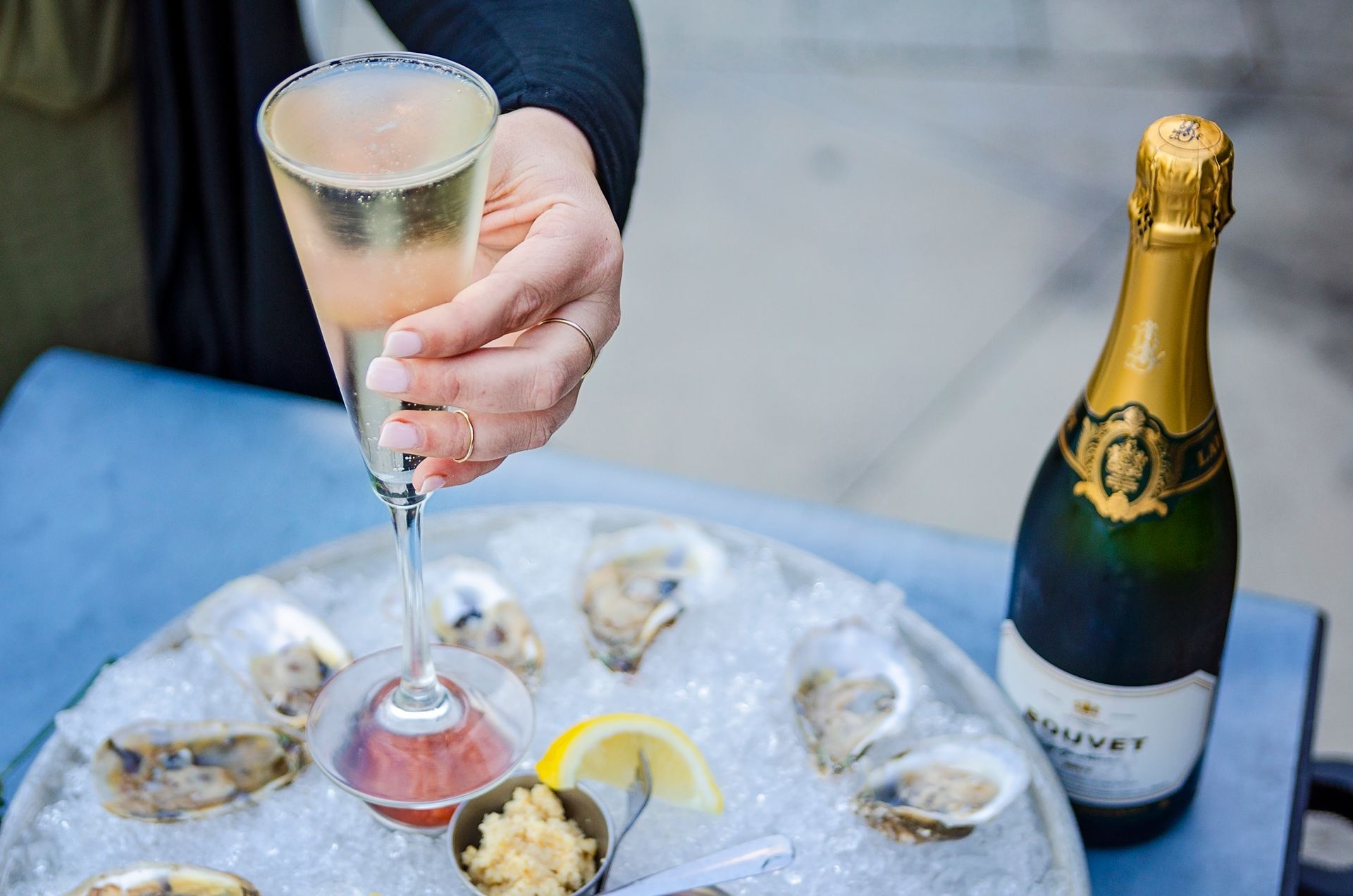 A person is pouring a glass of champagne over oysters on ice.
