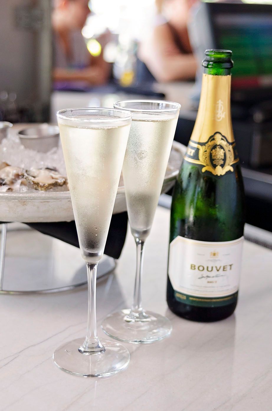 Two glasses of champagne and a bottle of Bouvet champagne on a table.