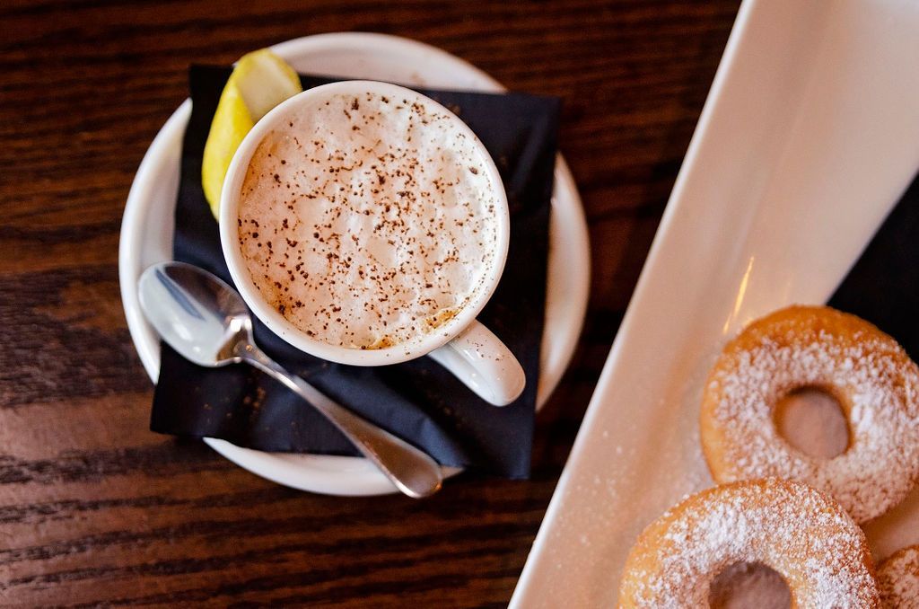 A cup of coffee next to a plate of donuts with powdered sugar on them