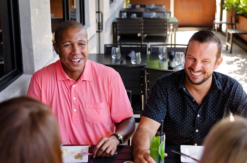 Two men are sitting at a table in a restaurant talking to each other.
