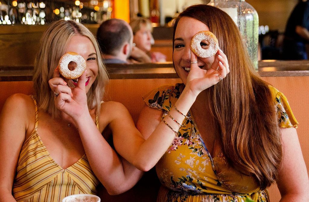 Two women are holding donuts in front of their eyes.