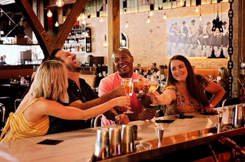 A group of people are sitting at a bar toasting with drinks.