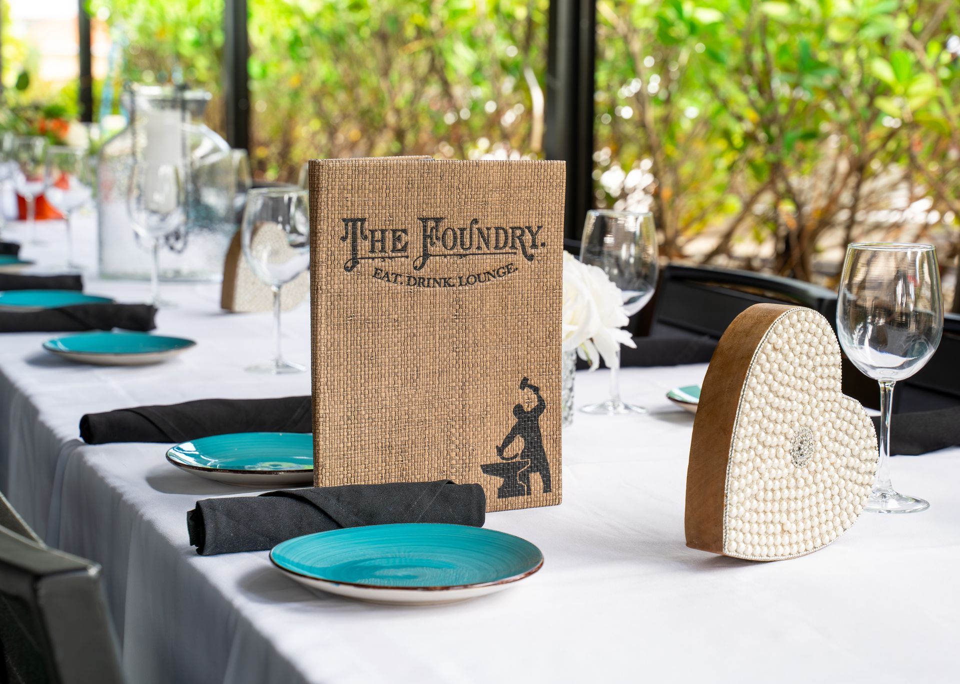 A long table with plates, glasses and a menu on it.