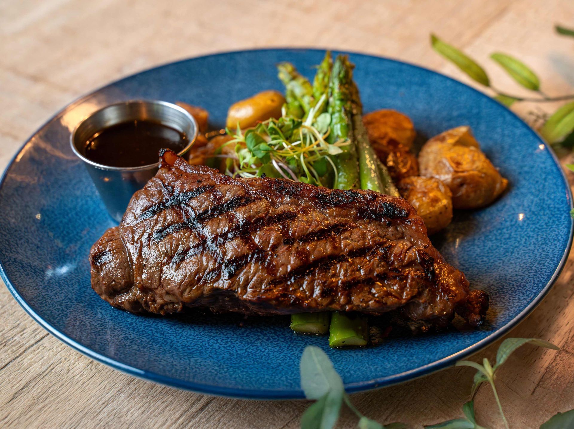 A blue plate topped with a steak, potatoes and asparagus.