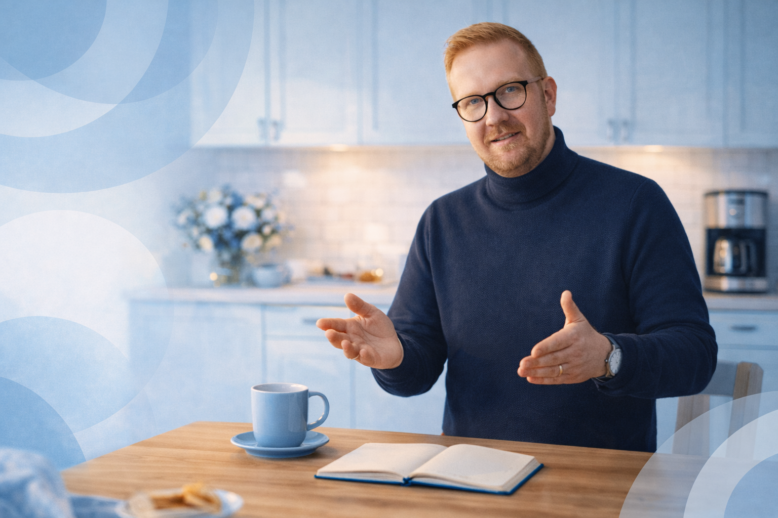 Een man met een bril gebaart, zittend aan een tafel met een kop koffie en een notitieboekje in een keukenomgeving.