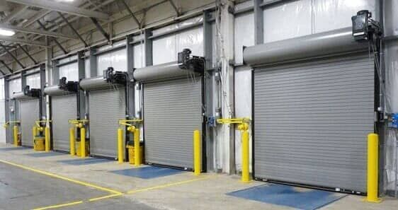 A row of garage doors in a warehouse with yellow poles.