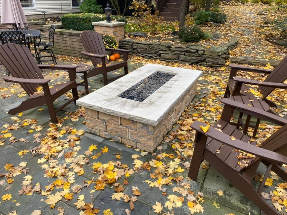 a fire pit is surrounded by chairs and leaves on a patio .