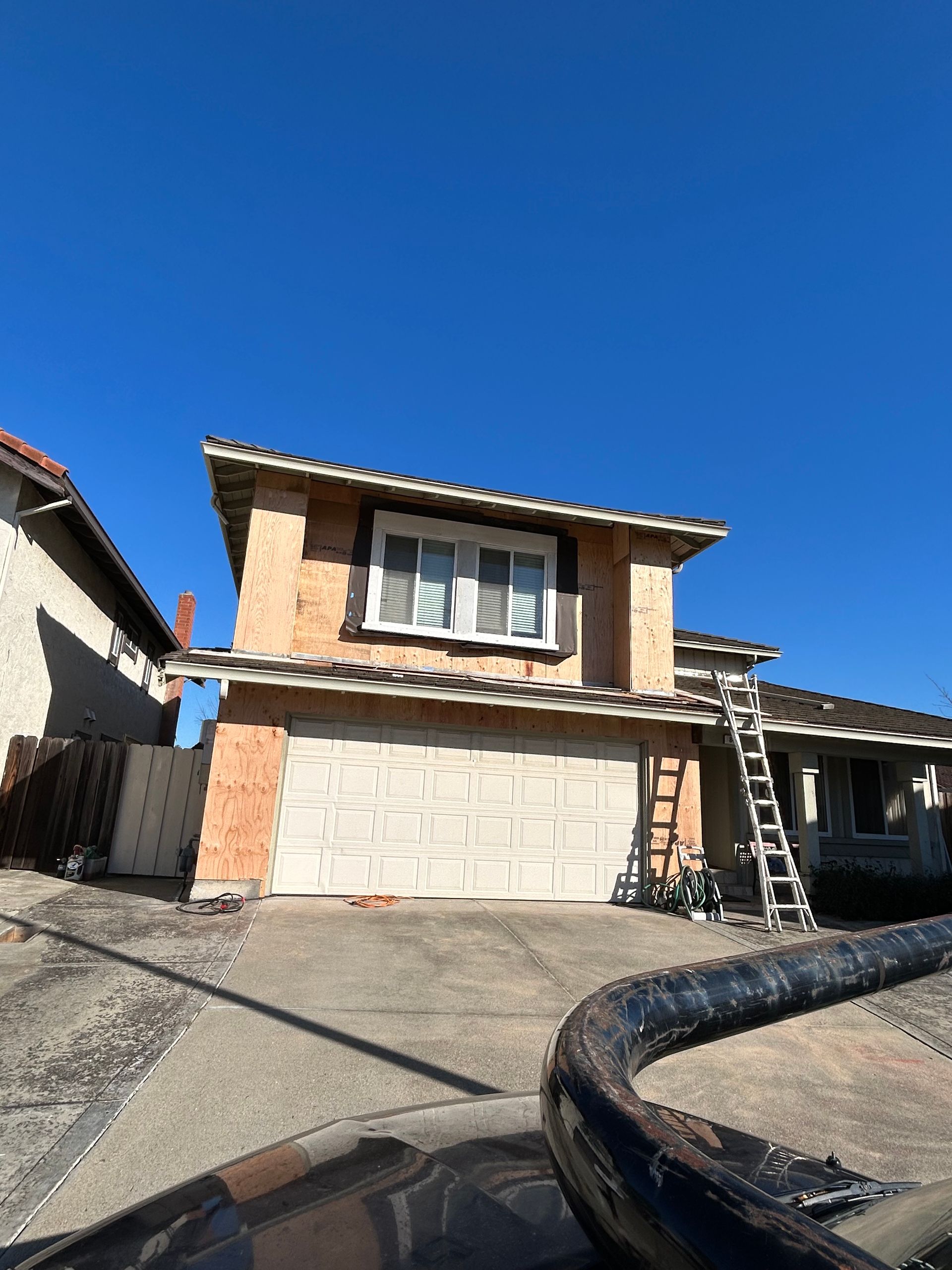 A beige two-story suburban house with a garage, under a clear blue sky, with a ladder leaning against the side.