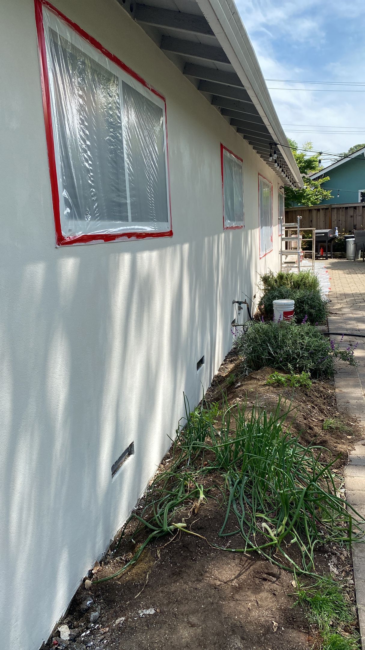 A white stucco house exterior with taped-off plastic covering the windows in preparation for painting.