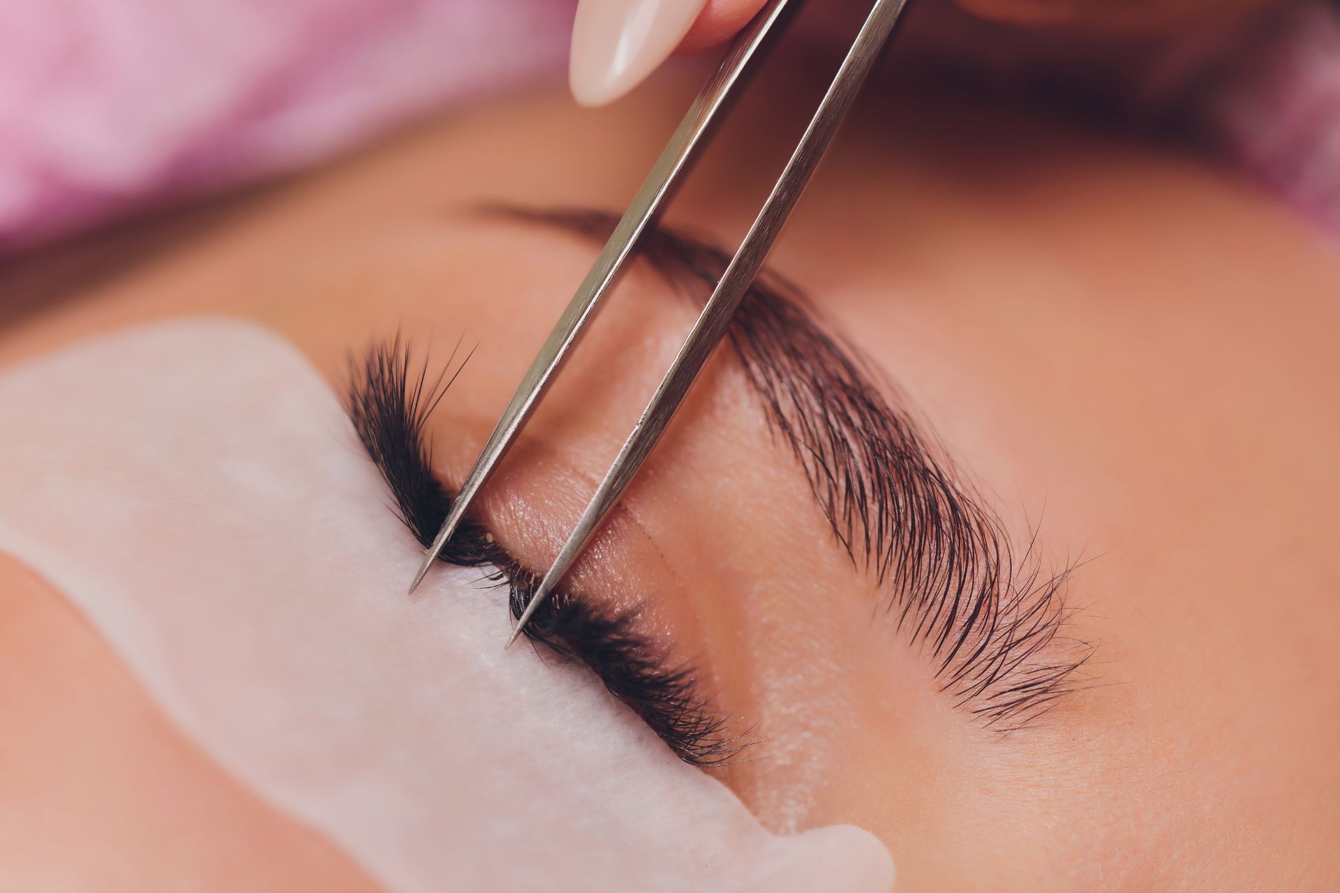 A woman is getting her eyelashes done with tweezers.