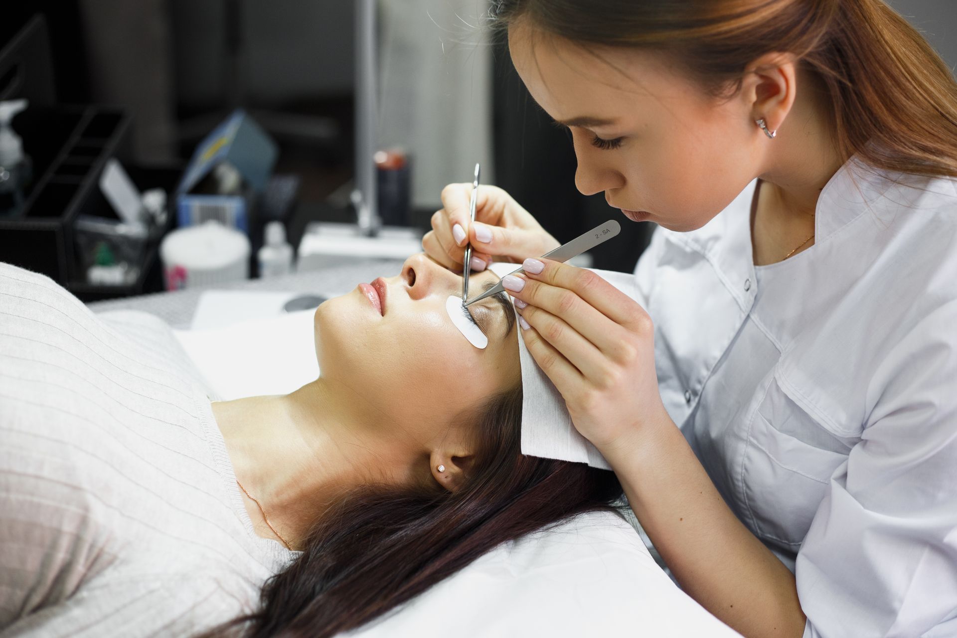 A woman is getting her eyelashes done by a woman in a beauty salon.