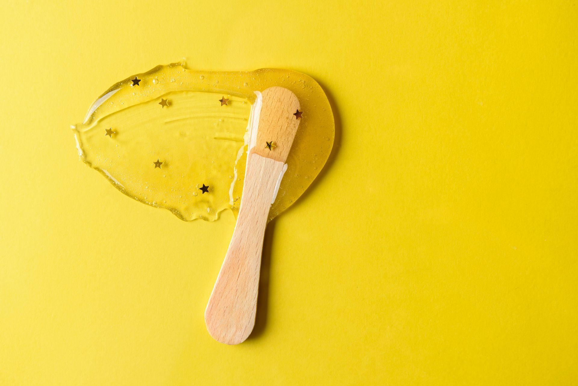 A wooden spoon with a piece of wax on it on a yellow background.
